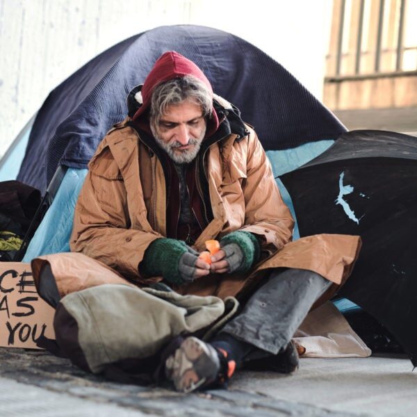 A homeless beggar man with a carboard sign sitting outdoors in city asking for money donation.